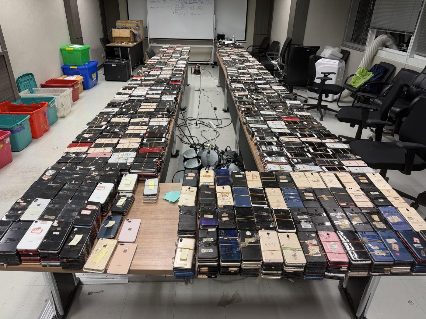 Long tables covered with hundreds of seized smartphones, bundled with rubber bands and labelled as evidence.